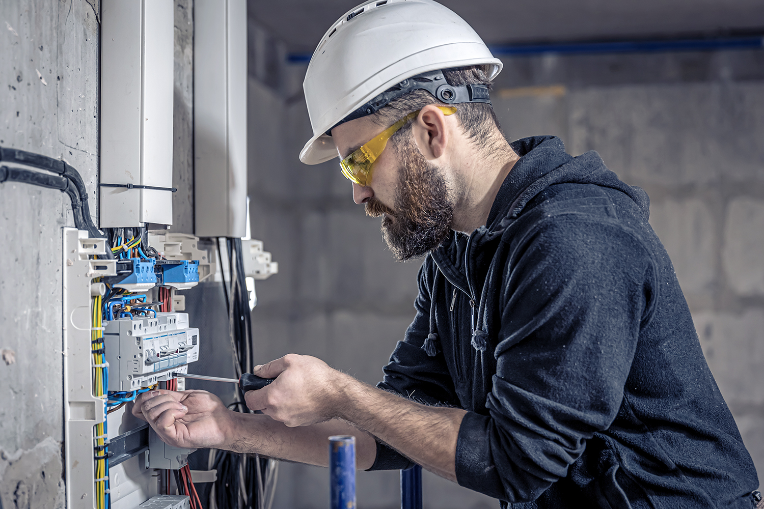 A male electrician works in a switchboard with an electrical connecting cable.